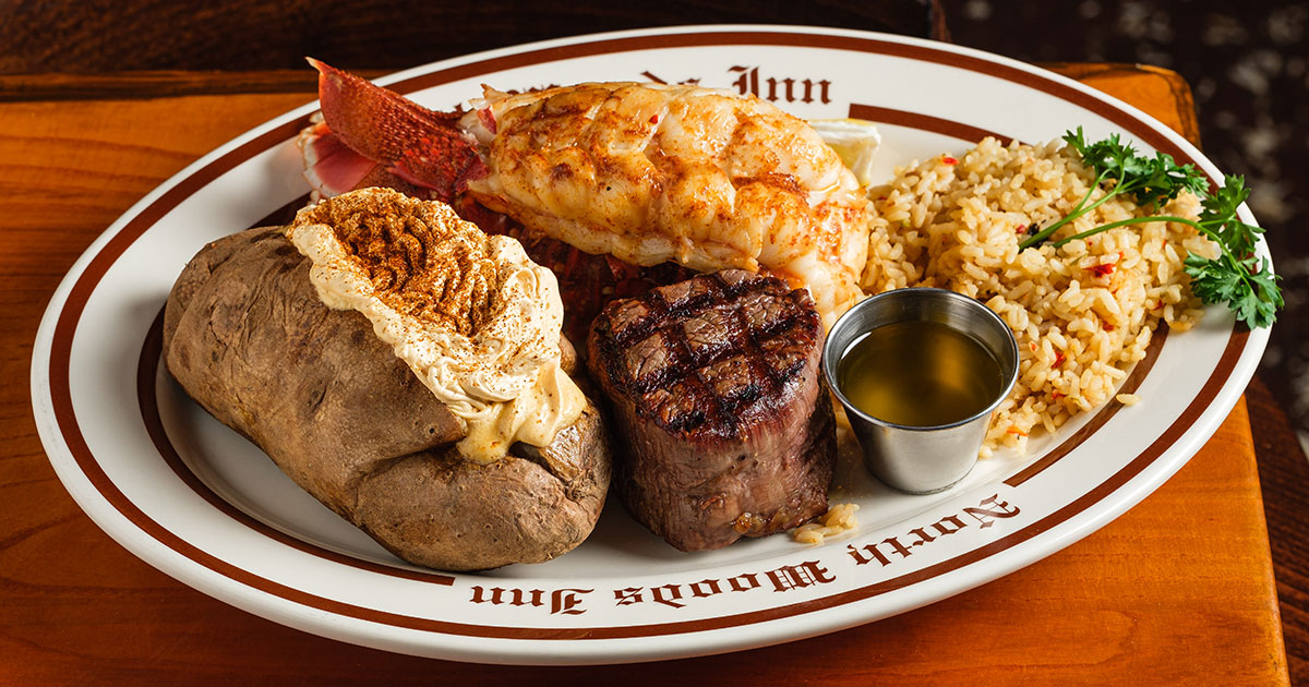 A filet mignon, lobster tail, baked potatoes, and rice on a North Woods Inn plate.